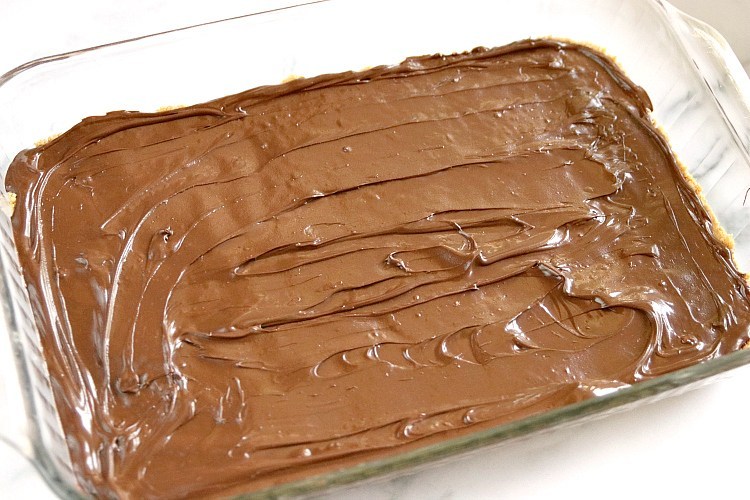 Spreading melted chocolate on the no bake peanut butter bars