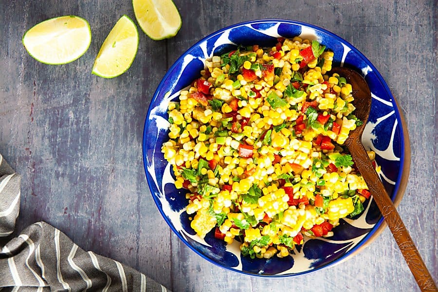 blue bowl of corn salad with three limes