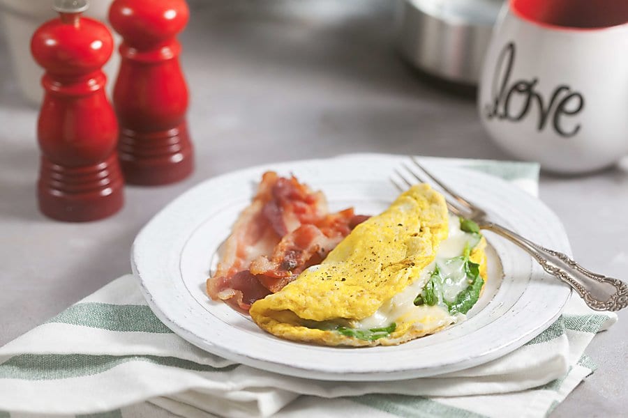 Overhead view of omelets with spinach on a gray plate with fresh berries and orange juice.