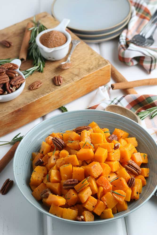 blue bowl full of roasted butternut squash cubes with ingredients in the background