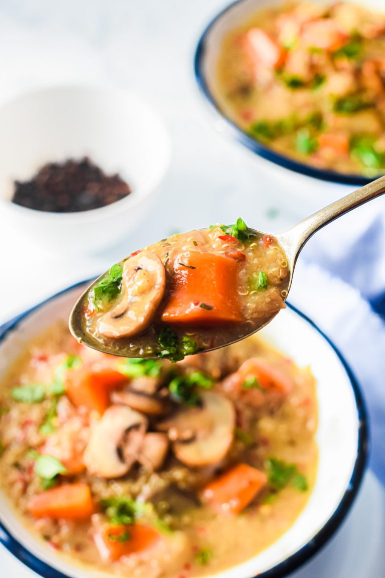 a spoon full of quinoa and mushroom soup above a bowl of soup